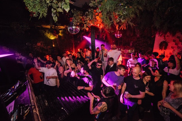 People dancing at a party with purple lighting and plants in the background